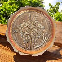 Photo of the round carnival glass platter outside in natural light showing the Iris flower pattern and herringbone background with iridescent tones.