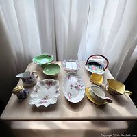 Overview of the miscellaneous vintage china grouping including various small plates, bowls, creamers and cups, all with floral decorations and varying colors.
