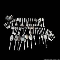 Full view of the assortment of silverplated flatware laid out on black background showing variety of pieces and patterns