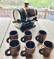 Photo showing the barrel-shaped ceramic decanter and six matching miniature mugs on a wooden table
