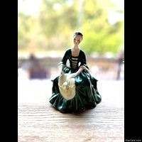 Front view of the Royal Doulton porcelain figurine of a seated woman in green colonial-style dress holding a bonnet.