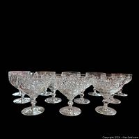 Set of 12 clear crystal Webb-Corbett Georgian pattern champagne/dessert glasses displayed on black background, showing cut crystal patterns and stems.