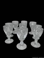 Nine clear crystal liqueur glasses in Georgian pattern arranged tightly together showing star and geometric cuts on a round foot and short stem.
