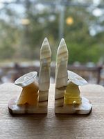 Front view of two alabaster bookends, showing pointed obelisk-like structures and flared funnel shapes mounted on a rectangular base with a blurred outdoor background.