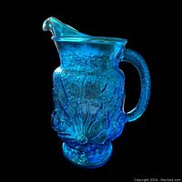 Side view of the aqua blue glass vintage pitcher showing its rain flower textured design, handle, and ice lip spout against black background.