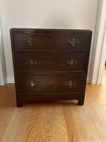 Front view of vintage wooden bedside dresser with three drawers and metal handles, showing the overall condition and design.