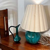 Jug and lamp on wooden surface showing size and color.