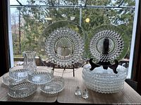 Full view of all glass dishes including large diamond point serving plates stacked, smaller coasters or side plates, crystal vase, and two crystal candleholders in front.