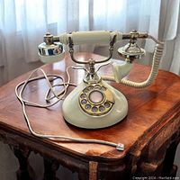 Full view of vintage ivory rotary dial telephone with brass accents on wooden table