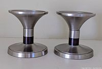 Pair of solid metal modern style candle holders with silver finish and black accent band. Shown side by side.