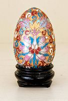Full view of the cloisonné champlevé egg with vibrant multi-color floral designs on a gold background displayed on a carved wood stand.