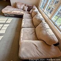 View of large L-shaped microfiber couch showing two-tone beige fabric and plush cushions positioned near window with sunlight.