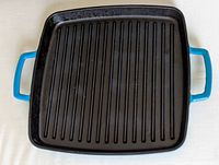 Top view of the black enamel interior grill pan with high ridges and teal enamel handles, square shape.