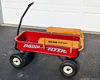 Side view of full Radio Flyer Big Red ATW wagon showing red metal body, wood side rails, large treaded wheels and bent black handle.