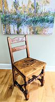 Full view of the vintage Stickley child's side dining chair showing the seat, ladder back, and spindle legs on a hardwood floor with part of a colorful painting in the background.