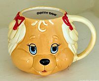 Front view showing Dotty Dog face mug with blue eyes, red ribbons, and handle.