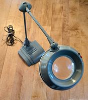 Front angled view showing the magnifying glass with integrated light, adjustable arm and heavy base of the lamp.