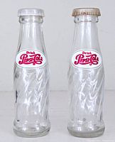 Pair of clear glass Pepsi-Cola shaped salt and pepper shakers, showing full front view with logo and caps.