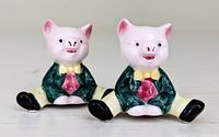 Front view of two ceramic pig salt and pepper shakers sitting with legs spread, wearing green jackets and yellow bow ties.