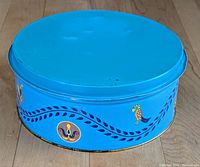 Closed view of large blue tin container with Pennsylvania Dutch decoration in folk art style, including bird and flower motifs on the side.
