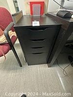 Front view of the black filing cabinet showing four drawers placed between office chairs and desks.