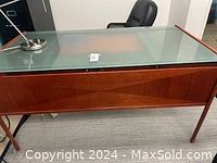 Full view of glass top desk showing wooden frame, legs, and attached metallic task lamp.