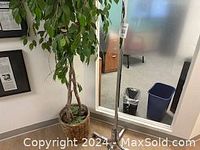 Photo showing an artificial potted tree with braided trunk in a wicker basket next to a metal coat rack.