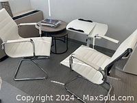 Two white side chairs with chrome cantilever frames, two nesting round coffee tables with dark wood tops and black metal bases, and a white adjustable desk with a chrome base.