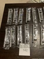 Seventeen metal 6-inch kitchen cabinet handles individually wrapped in clear plastic packaging with screws included, laid out on dark surface.