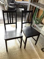 Two black IKEA kitchen chairs with straight legs and three vertical slats in backrests, placed on a metal floor.