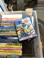Photo showing a clear plastic container with children's DVDs and Blu-rays, cover of 'Rio' Blu-ray visible on top.