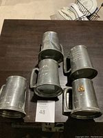 Five pewter mugs arranged on a table, showing overall condition and size with a lot card labeled 48.