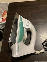 Side view of the Hamilton Beach electric iron showing the white and teal body with control dial and cord