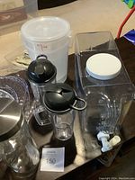 Photo showing 2 large plastic drink containers, two smaller pitchers with black tops, and a large measuring container.