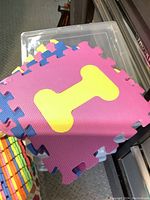 Top view of stack of colorful interlocking foam play mats showing a pink mat with yellow bone shape and blue edges.