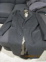 Full view of men's long charcoal gray coat with two-button closure, laid out on a couch.