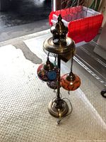 Full view of the Turkish lamp showing three hanging mosaic glass orbits and metal stand on a textured floor.