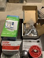 Photo of HydroRight dual flush valve box, Moen loose parts box, Master Plumber gasket set, and chrome sink stopper on floor.