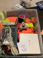Top view of assorted tools, LED bulbs, tape dispenser, and safety vests in a clear plastic container.