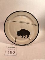 Front view of cream stoneware side plate with black painted bison silhouette and horizontal line design on surface, showing overall condition and design.