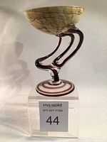 Front view of the artistic glass goblet on a clear acrylic stand with auction lot label visible.
