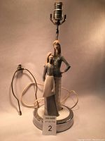Full view of the porcelain figurine lamp showing the mother and daughter on the metal base with electrical components and power cord.