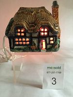 Front view of the thatch cottage night light illuminated showing warm light through windows and door.