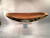 Side view of wooden dough bowl showing natural wood color and one carved painted white rose with green leaves.