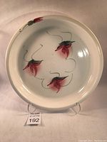 Full view of circular white stoneware platter with red and green floral design on cream gloss surface.