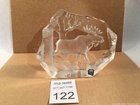 Front view of crystal glass moose sculpture showing engraved and sandblasted moose and natural background design with the artist label visible at bottom right.