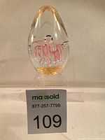 Front view of clear teardrop Murano art glass paperweight with pink swirls and visible controlled bubbles with gold flecks at the base.