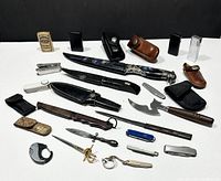 Group image showing collection of knives, box cutters, and Zippo lighters arranged on a white surface with black background