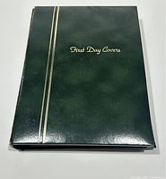 Closed green album with gold lettering 'First Day Covers' and gold stripes on the left side.