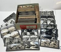 Box containing approximately 180 vintage black and white stereoscope stereo-view cards arranged in stacks, showing a variety of scenes from landscapes to industrial and group views.